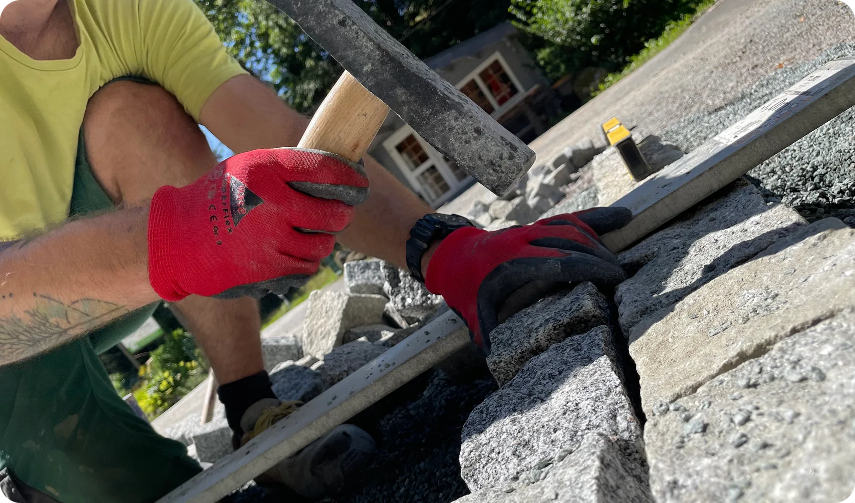 Hände mit Arbeitshandschuhen setzen Granitpflaster mit Hammer und Richtlatte
