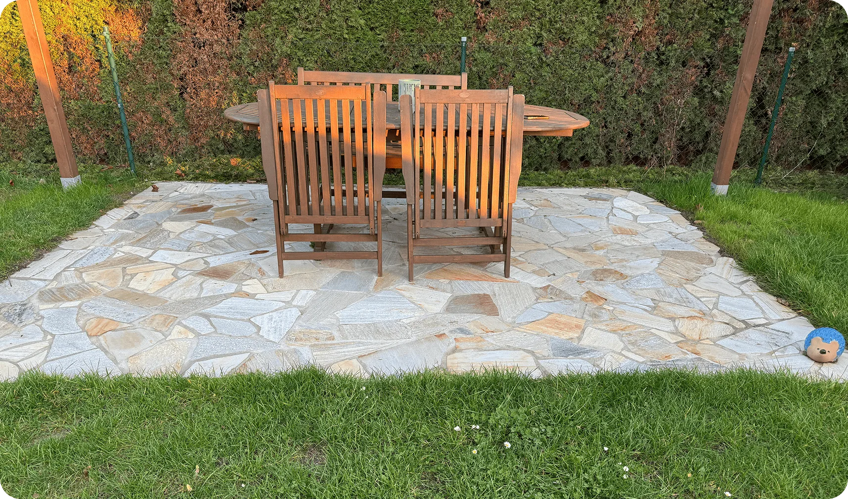 Terrasse aus Polygonalplatten im Rasen mit Holztisch und Gartenstühlen