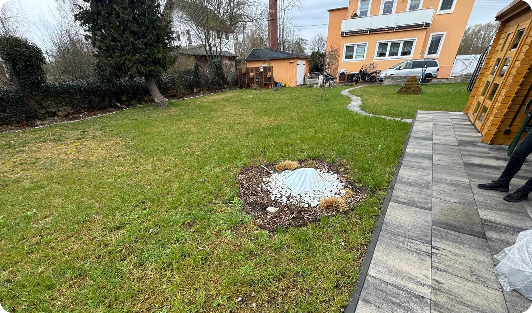 Vorher: Rasenfläche mit Schachtabdeckung neben einer grauen Terrasse