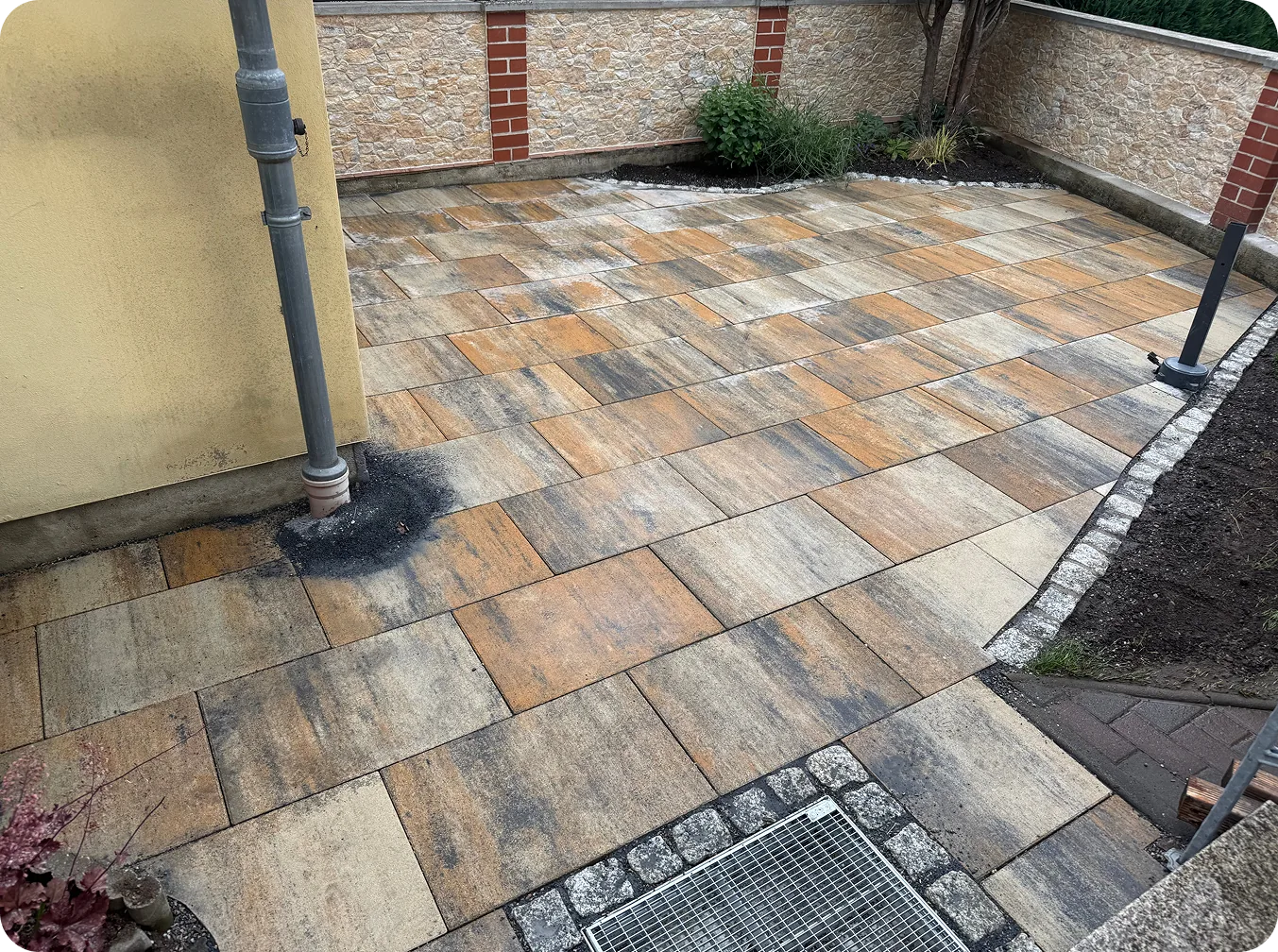 Neue Terrasse aus mehrfarbigen Betonplatten mit Granitpflaster an einer Mauer