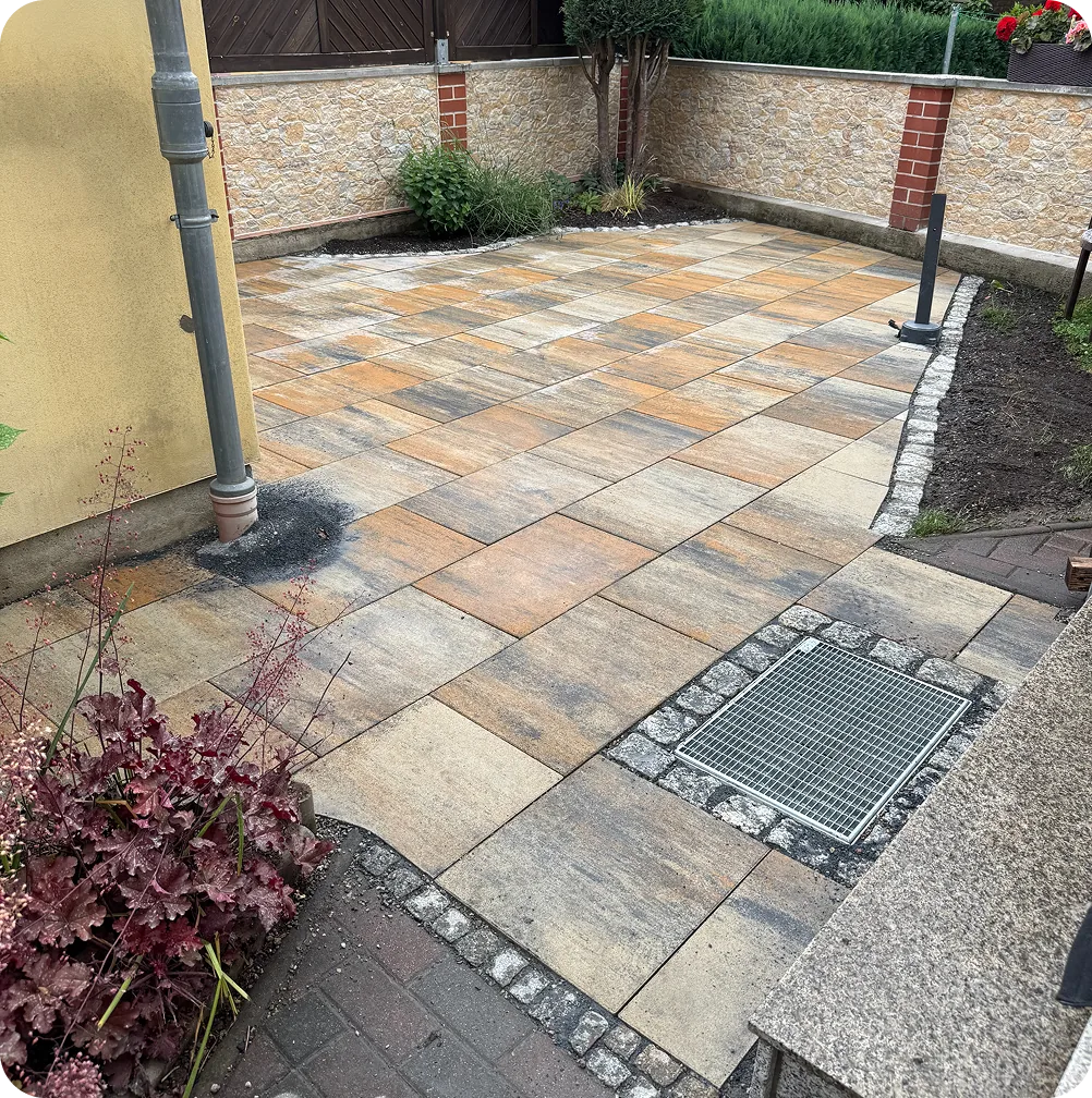 Fertige Terrasse aus Betonplatten mit Granitrand, Gitterrost und Purpurglöckchen